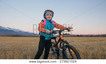 One Caucasian Children Walk With Bike In Wheat Field. Little Girl Walking Black Orange Cycle On Back
