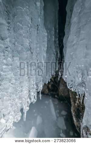 Winter Baikal. Olkhon Island. Ice Grotto. Thick Blue Ice And Icicles On The Coastal Rocks Of Olkhon 