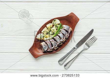 Top View Of Marinated Herring, Potatoes And Onions In Earthenware Plate With Glass Of Vodka And Cutl