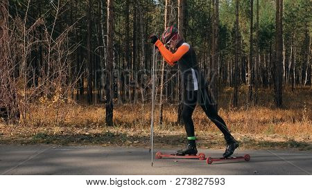 Training An Athlete On The Roller Skaters. Biathlon Ride On The Roller Skis With Ski Poles, In The H