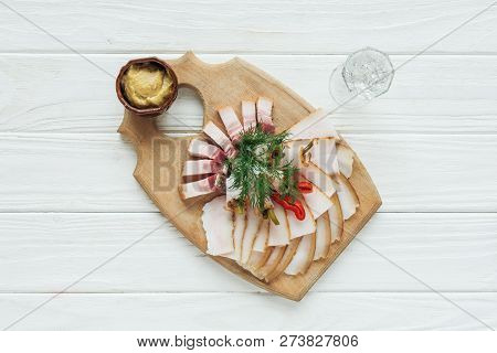 Top View Of Traditional Sliced Smoked Lard On Cutting Board With Mustard And Glass Of Vodka On White