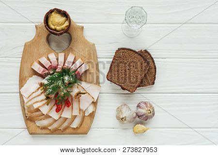 Top View Of Traditional Sliced Smoked Lard On Cutting Board With Mustard, Glass Of Vodka And Rye Bre