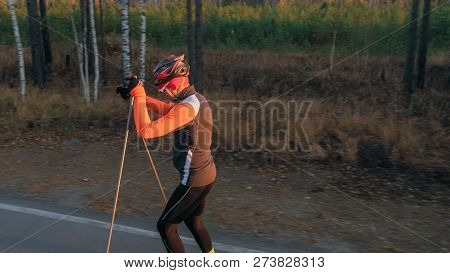 Training An Athlete On The Roller Skaters. Biathlon Ride On The Roller Skis With Ski Poles, In The H