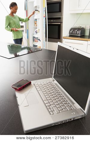 Junge Frau, die Festsetzung von Snack In Küche mit Laptop In moderne Küche