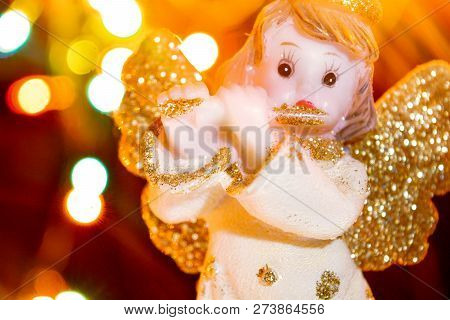 Figurine Of Little Angel With Golden Shiny Wings And Halo That Plays Flute On Shining Background Of 