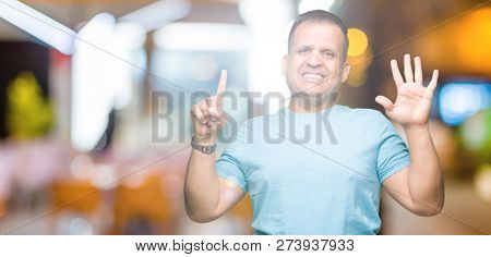 Middle age arab man wearing blue t-shirt over isolated background showing and pointing up with fingers number six while smiling confident and happy.