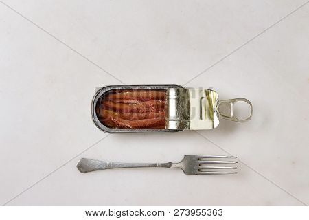 Pickled Salted Anchovies Fillet In Oil In Open Tin Can With Fork Over White Marble Background. Flat 