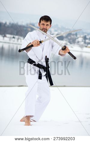 The Fighter In White Kimono Is Practicing Martial Arts With Two Swords Shoeless On Snow At Winter.