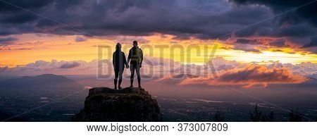 Fantasy Adventure Composite Of A Man And Woman Couple On A Rocky Mountain Peak During A Colorful Dra