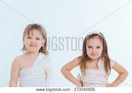 A Little Girls Grimaces Against A White Background. The Children Is Up To Something. Concept Of Emot