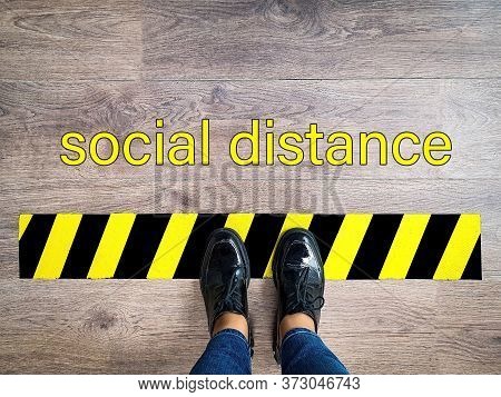 Person Stands In Line With Yellow And Black Stripes Keeping Safe Social 1m Distance Due To Pandemic.