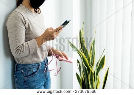Young Women In Mask Leaning Against The Wall Playing With Smartphone While Charging The Smartphone B