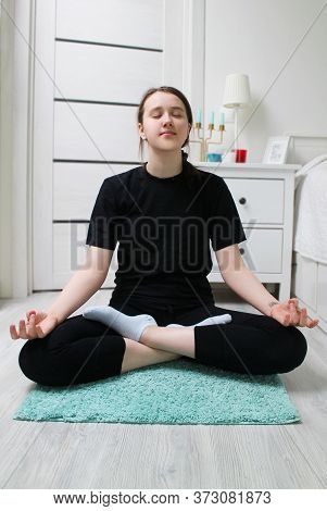 The Girl Is Sitting In The Lotus Position, Doing Yoga At Home. The Concept Of Yoga Classes As An Opp