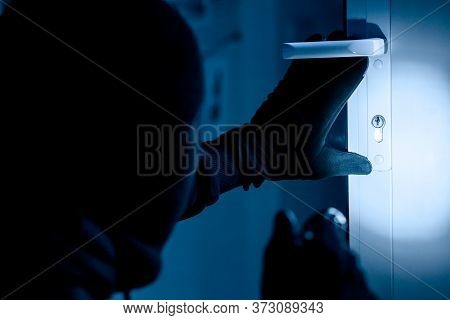Vandalism Concept. Rear View Of Disguised Burglar Entering Enclosed Property, Holding Flash Light, L