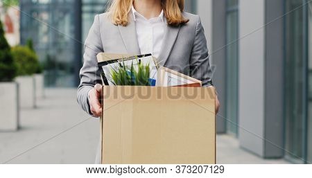 Portrait Of Caucasian Sad Businesswoman In Glasses Standing Outdoors With Box Of Stuff. Leaving Busi
