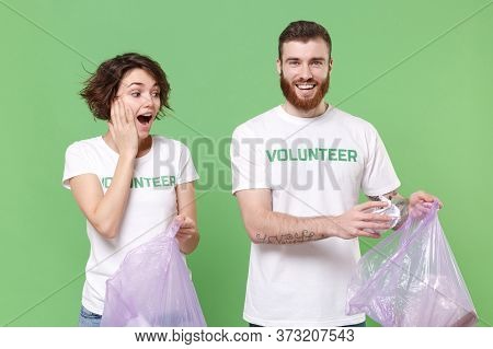 Shocked Friends Couple In Volunteer T-shirt Isolated On Green Background. Voluntary Free Work Assist