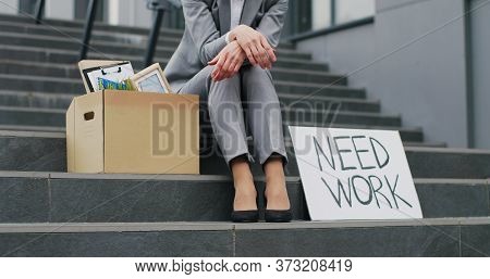 Portrait Of Caucasian Young Unemployed Woman Sitting Outdoors At Stairs With Poster Need Work. Femal