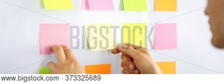 A Man Stands In The Office And Glues Small Notes On The Wall. Multicolored Stickers On A Glue Basis.