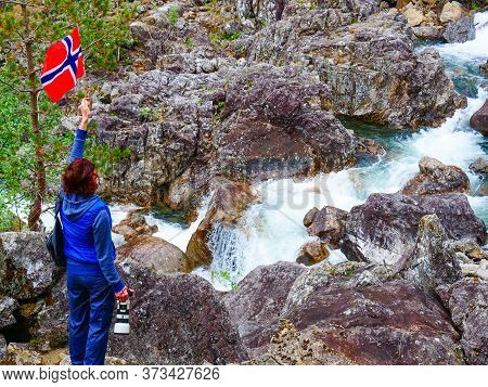 Tourist Woman With Norwegian Flag And Camera Walking Trough Mountains Path In Allmannajuvet Area Sau