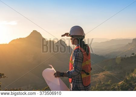 Engineer Asian Man With Long Hair Wearing A White Helmet Holding Blueprint And Looking At Sunset On 