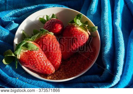 Three Strawberries And Sugar Cane On Blue Cloth Background In White Bowl