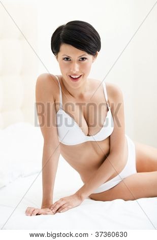 Halfnaked kvinde sidder på en bred seng, isoleret på hvid baggrund