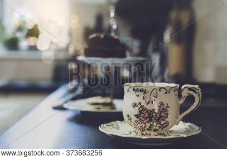Hot Cup Of Tea With Blurry Cake On Hight Tea Stand In The Kitchen Background. Cup Of Aroma Dring Wit