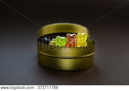 Closeup Of Three Jelly Bears Peeping Out Of A Round Tin Candy Box On Brown Background. Selective Foc