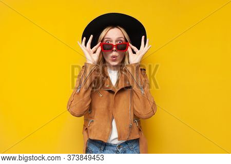 Shocked Girl In Autumn Clothes And Glasses Is Surprised At A Yellow Isolated Background, A Woman Tak