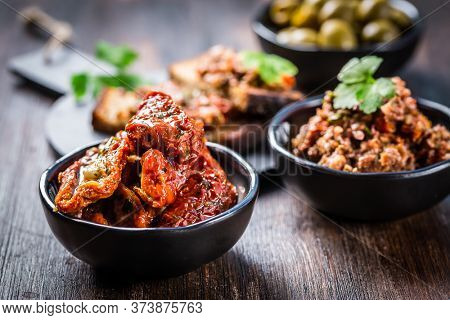 Sun dried tomato with olive oil as antipasto with tapenade and bruschetta in background