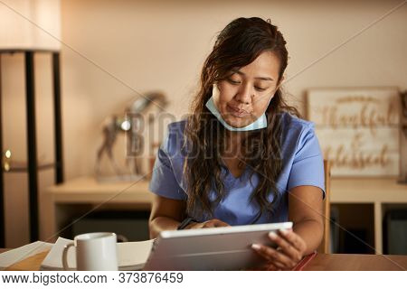 filipina nurse working from home doing paperwork and using tablet