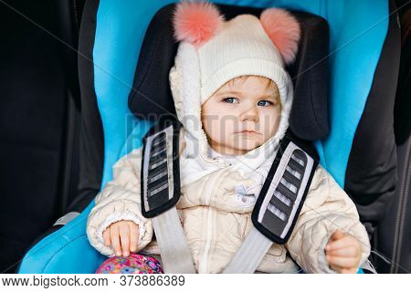 Adorable Baby Girl With Blue Eyes Sitting In Car Seat. Toddler Child In Winter Clothes Going On Fami