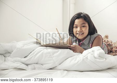 Asian Children Writing Letter On Diary Book. Kid Learn And Work, Read Book, Girl Lying In White Bedr