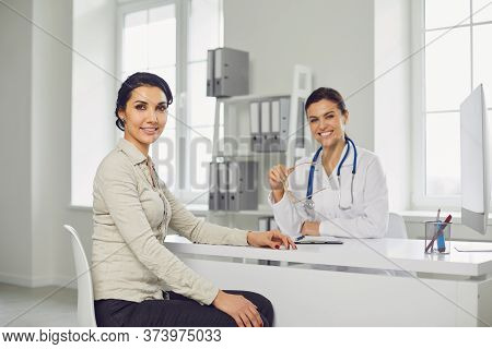 Smiling Female Patient At Consultation With Woman Doctor Sitting At Table In Office Clinic.