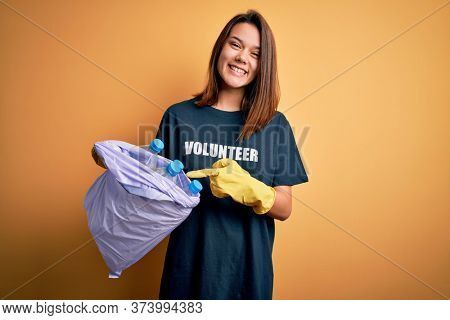 Beautiful volunteer girl caring environment doing volunteering holding bag with rubish bottles very happy pointing with hand and finger