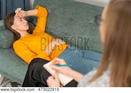 Young Woman Is Undergoing Therapy With A Female Psychologist. She Is Lying On The Couch And Is Very