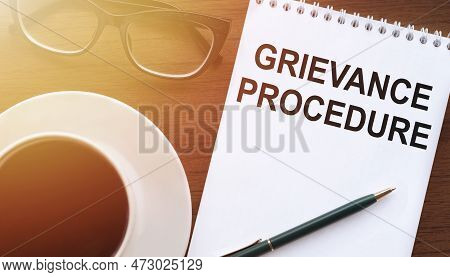 Grievance Procedure Text On Notebook On Office Table With Cup Of Coffee