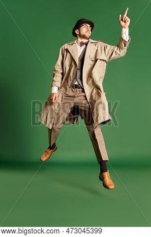 Portrait Of Young Handsome Man, In Image Of Detetive In Stylish Trench Coat And Hat Posing Against G