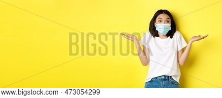 Covid-19, Quarantine And Social Distancing Concept. Clueless Asian Woman In Medical Mask Shrugging S