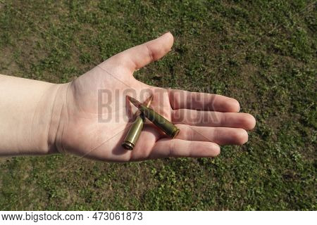 Two Rifle Cartridges In Hand Against The Background Of Green Grass. Close-up
