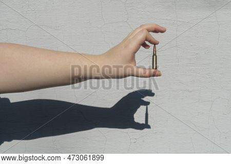 Rifle Cartridge In Hand Against The Background Of A White Concrete Wall. A Shadow Forms On The Wall
