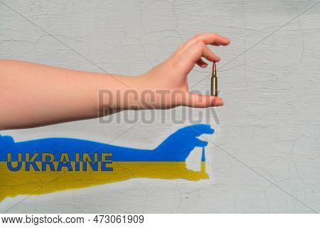 Rifle Cartridge In Hand On The Background Of The Wall. Shadow Of Yellow-blue Color With The Inscript