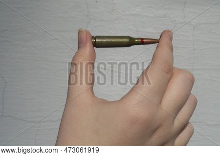 Rifle Cartridge In Hand Against The Background Of A White Concrete Wall. Close-up