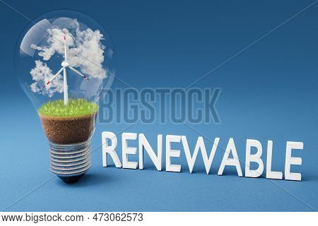 Single Lightbulb With Minature Wind Turbine Inside; Green Soil And Clouds; Renewable Energy Concept;