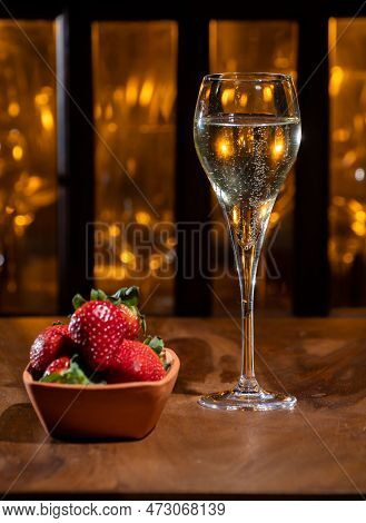 Glass Of Brut Champagne Bubbles Wine In Tulip Glass And Bowl With Fresh Strawberries On Evening Bar