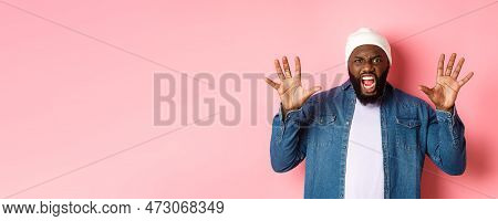 Angry African-american Guy In Beanie, Scare You, Roaring And Screaming, Showing Hands, Standing Ove 