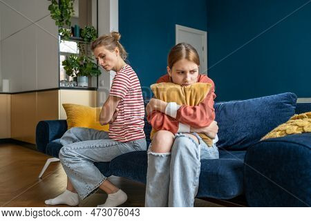 Upset Teenage Daughter And Young Woman Mother Sitting Separately In Silence On Sofa At Home, Feeling