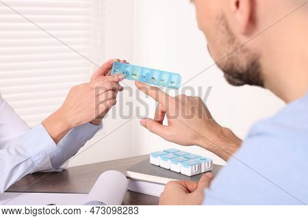 Doctor Holding Box Of Pills And Consulting Patient At Table In Clinic, Closeup