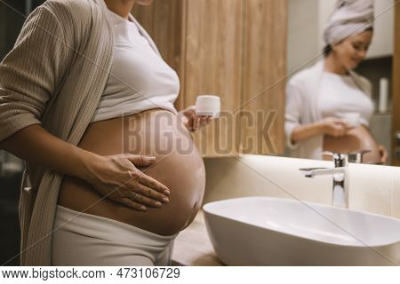 Cropped Picture Of A Pregnant Woman Putting On Anti-stretchmarks Lotion On Her Tummy In A Bathroom.