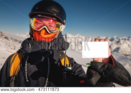 Snowboarder Holds An Empty Lift Pass With A Mountain In The Background. Blank Ski Pass In The Hand O